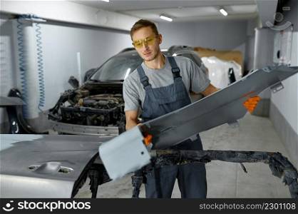 Mechanic taking freshly painted auto body part. Car assembly after painting. Repair service. Mechanic engaged auto part assembly after painting