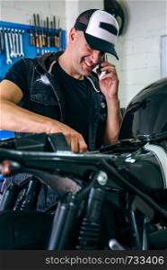 Mechanic talking on the phone while fixing the motorbike. Mechanic talking phone while fixing motorbike