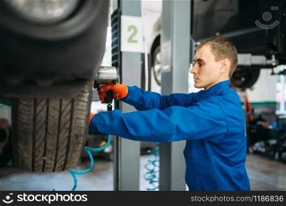 Mechanic unscrews the wheel with a pneumatic wrench. Car service, automobile repair. Mechanic unscrews the wheel with pneumatic wrench