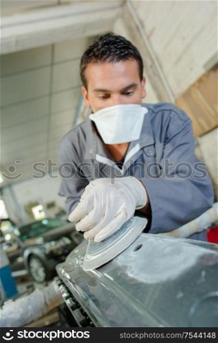Mechanic using circular machine on car panel