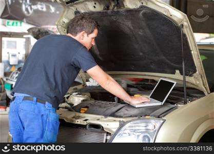 Mechanic using laptop while repairing car in garage