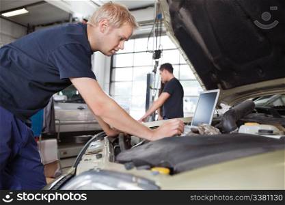 Mechanic using laptop while working on car with people in background