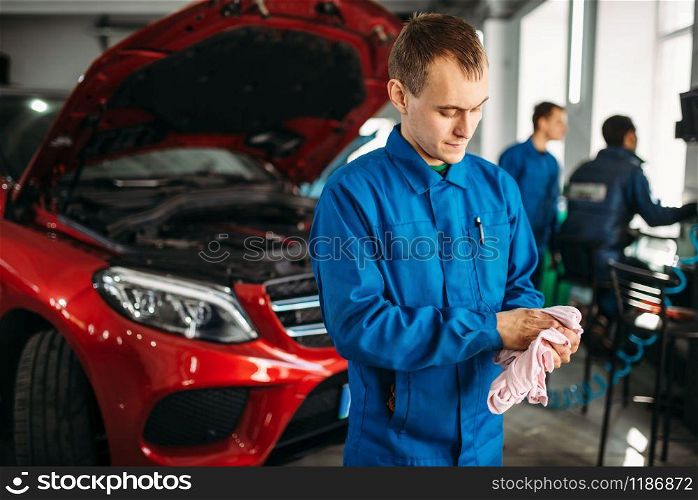 Mechanic wipes his hands after repairing the car, motor diagnostic. Vehicle with opened hood on background, auto-service. Mechanic wipes his hands after repairing the car