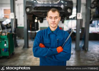 Mechanic with a wrench in hands, car on the lift on background, repair station. Tire service, vehicle maintenance