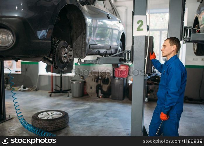 Mechanic with a wrench in hands looks at the car on the lift. Tire service, vehicle maintenance, repair station