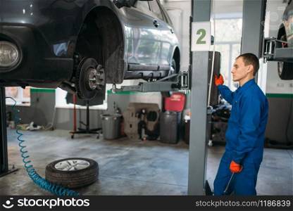 Mechanic with a wrench in hands looks at the car on the lift. Tire service, vehicle maintenance, repair station