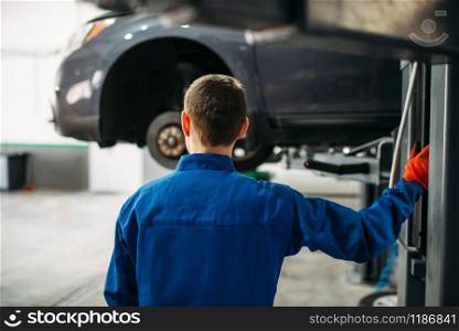Mechanic with a wrench in hands looks at the car on the lift. Tire service, vehicle maintenance, repair station. Mechanic with wrench looks at the car on lift