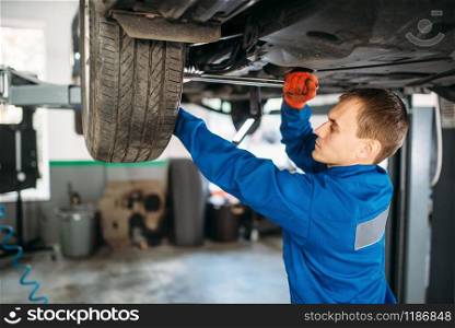 Mechanic with a wrench repairs the suspension, car on the lift. Tire service, vehicle maintenance. Mechanic repairs the suspension, car on the lift