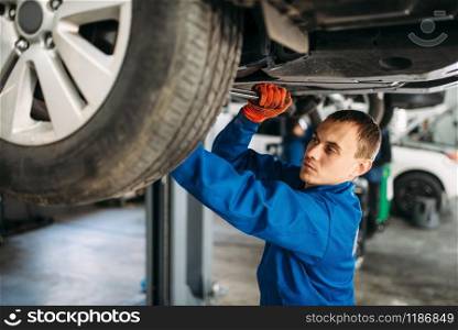 Mechanic with a wrench repairs the suspension, car on the lift. Tire service, vehicle maintenance