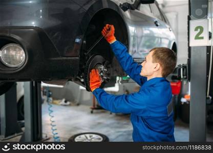 Mechanic with a wrench repairs the suspension of the car. Tire service, vehicle maintenance. Mechanic with wrench repairs the suspension of car