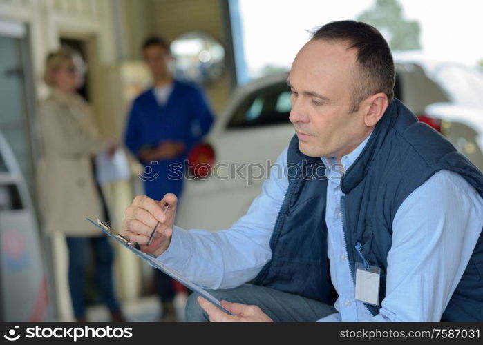 mechanic with clipboard customer waiting in background