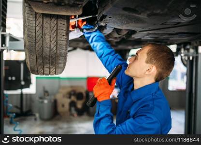 Mechanic with lamp checks the car suspension, repair station. Tire service, vehicle maintenance