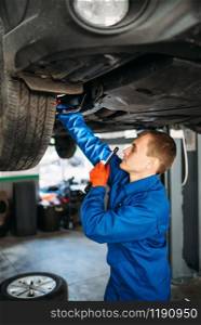 Mechanic with lamp checks the car suspension, repair station. Tire service, vehicle maintenance. Mechanic with lamp checks the car suspension