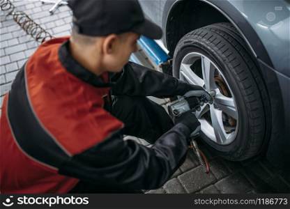 Mechanic with pneumatic wrench unscrews the wheel in tire service. Man repairs car tyre in garage, automobile inspection in workshop