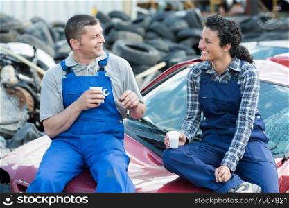 mechanics having coffee sat on scrap car
