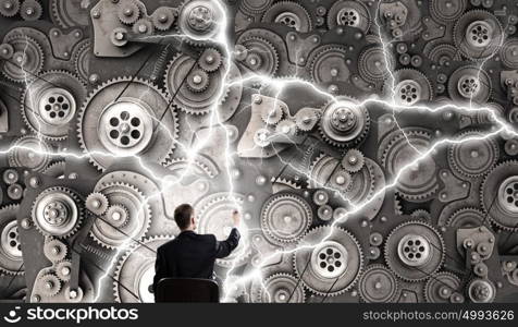 Mechanism of teamwork and collaboration. Young relaxed businessman sitting in chair and looking at gears mechanism