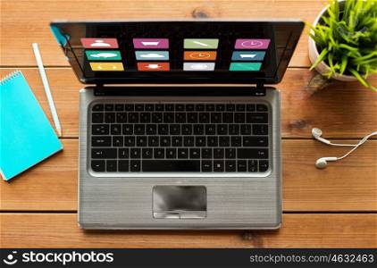 media, education, business and technology concept - close up of laptop computer with menu icons on screen on wooden table