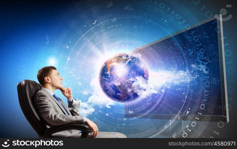 Media technologies. Young businessman sitting in chair behind tv. Elements of this image are furnished by NASA