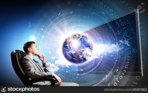 Media technologies. Young businessman sitting in chair behind tv. Elements of this image are furnished by NASA