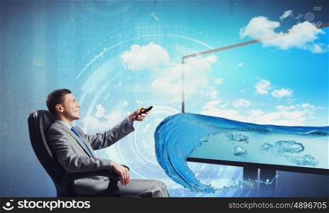 Media technologies. Young businessman sitting in chair behind tv with click in hand