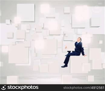 Media technologies. Young smiling businessman sitting on white cube