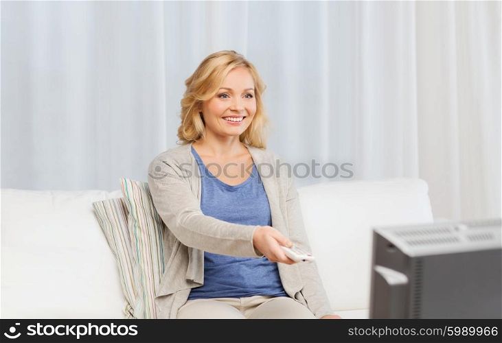 media, technology, leisure and people concept - smiling middle aged woman with remote control switching tv at home