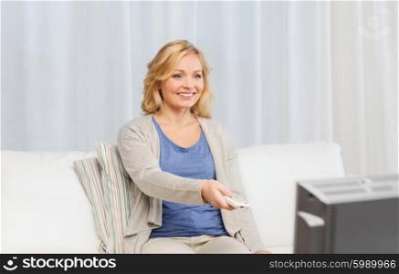 media, technology, leisure and people concept - smiling middle aged woman with remote control switching tv at home