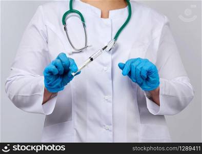 medic woman in white coat and blue latex gloves holds a syringe, white studio background, vaccination concept