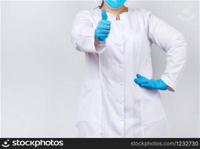 medic woman in white coat and mask, wearing blue medical latex gloves on her hands, showing like gesture in hand, approval concept, copy space