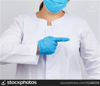 medic woman in white coat with buttons on her hands, wearing blue sterile gloves, showing hand gesture indicating the subject, white background