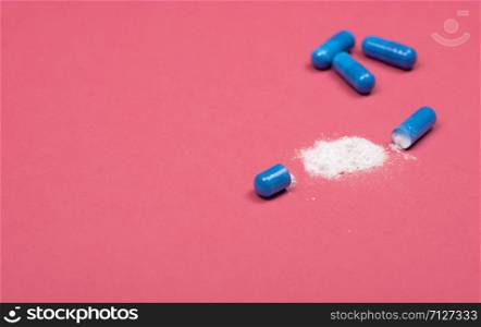Medical background. Open blue capsule pill on pink background. Blue capsules pill spread on fuchsia background with copy space.. Medical background. Open blue capsule pill on pink background