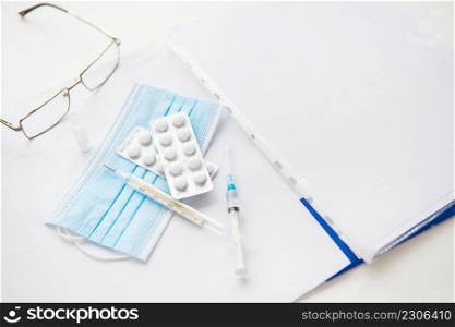 Medical background: pills, glasses, pen, mask, thermometer, vaccine, syringe and papers with patient data. Medical theme. Concept: vaccination against coronavirus. Medical background: pills, glasses, pen, mask, thermometer, vaccine, syringe and papers with patient data. Medical theme. Concept: vaccination against coronavirus.