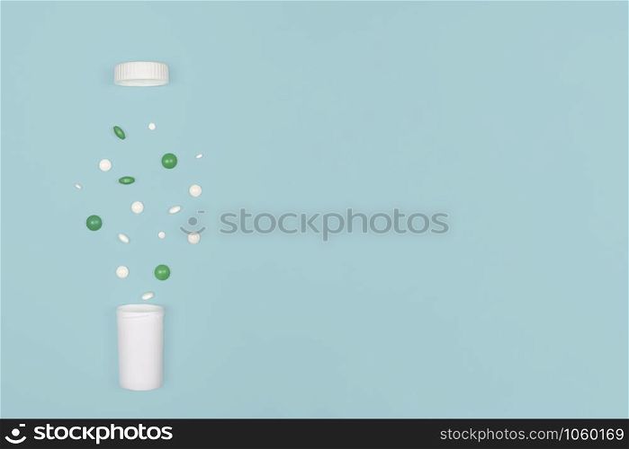 Medical background with pills. White and green pills pour out of a bottle on a blue background. Flat lay concept. Copy space.. Medical background with pills and bottle.