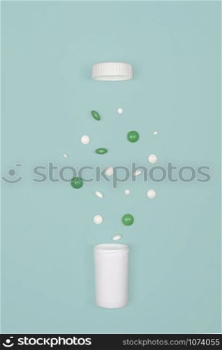 Medical background with pills. White and green pills pour out of a bottle on a blue background. Flat lay concept.. Medical background with pills and bottle.
