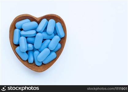 Medical blue pills with heart shaped wooden bowl on white background. Copy space