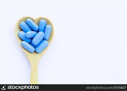 Medical blue pills with heart shaped wooden spoon on white background. Copy space