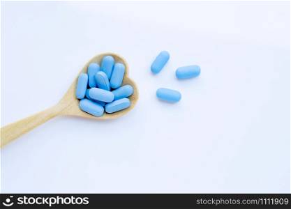 Medical blue pills with heart shaped wooden spoon on white background. Copy space