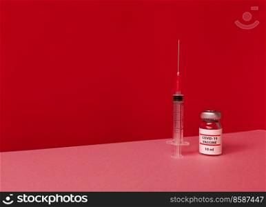 Medical bottle with covid 19 vaccine and syringe on a red backdrop with tilted trendy skyline and copy space.. Medical bottle with covid 19 vaccine and syringe on red backdrop with tilted trendy skyline and copy space.