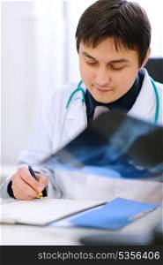 Medical doctor analyzing patients roentgen and writing results in clipboard&#xA;