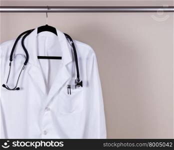 Medical Doctor Consultation white coat with pens and stethoscope hanging on rack with off white wall in background. Horizontal layout with copy space.