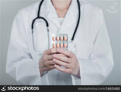 Medical doctor holding strip of pills on grey hospital wall background. Antibiotics and virus treatment tablet.