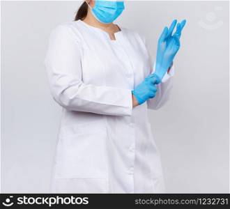 medical doctor in a white coat and mask puts on medical hands latex gloves before procedures, white studio background