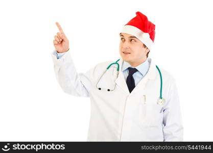 Medical doctor in hat of Santa Claus pointing finger in corner at copy space isolated on white&#xA;