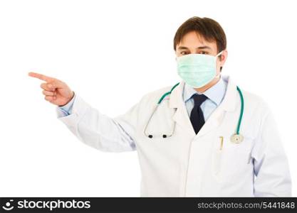 Medical doctor in mask pointing finger up in corner at copy space isolated on white&#xA;