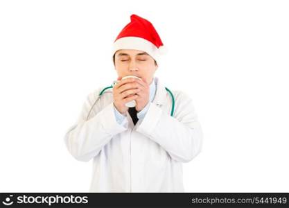 Medical doctor in Santa hat enjoying cup of hot coffee isolated on white&#xA;