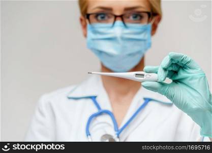 medical doctor nurse woman wearing protective mask and gloves - holding electronic thermometer.. medical doctor nurse woman wearing protective mask and gloves - holding electronic thermometer