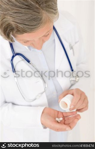 Medical doctor senior female holding pills looking down smiling portrait