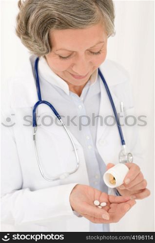 Medical doctor senior female holding pills looking down smiling portrait
