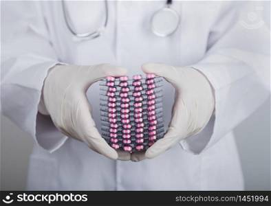 Medical doctor wearing clear latex gloves holding stack of different pills on grey hospital wall.