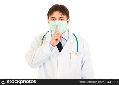 Medical doctor with mask on face holding finger at mouth isolated on white. Shh gesture&#xA;